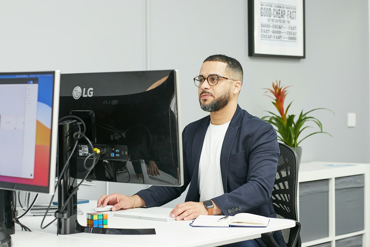 A professional seated at his desk in a bright office, glancing calmly away from his computer.