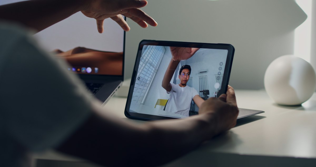 A hand holding a tablet that shows a live video session.